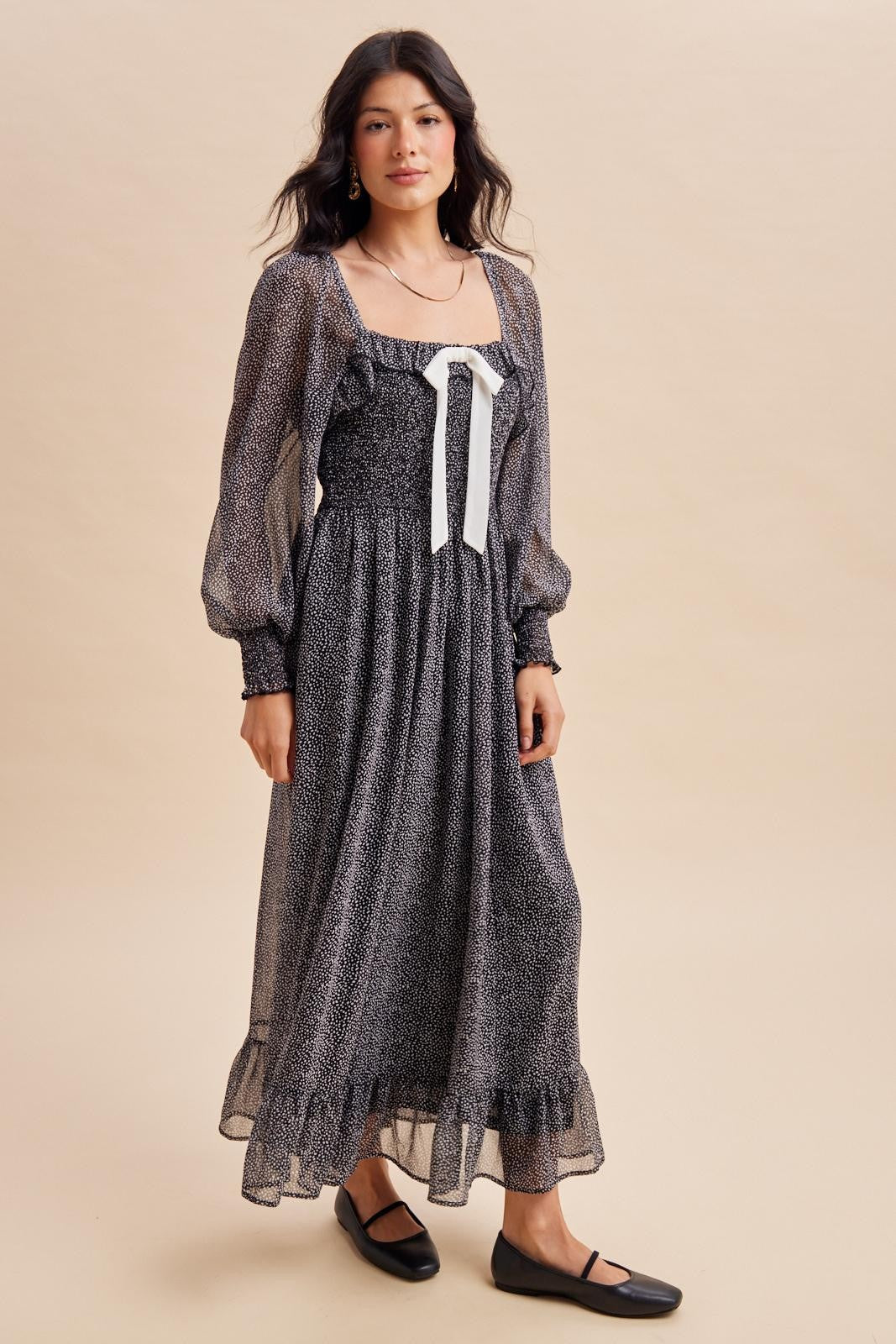 woman wearing a black and white spotted maxi dress with puff sleeves and a ribbon detail at the front