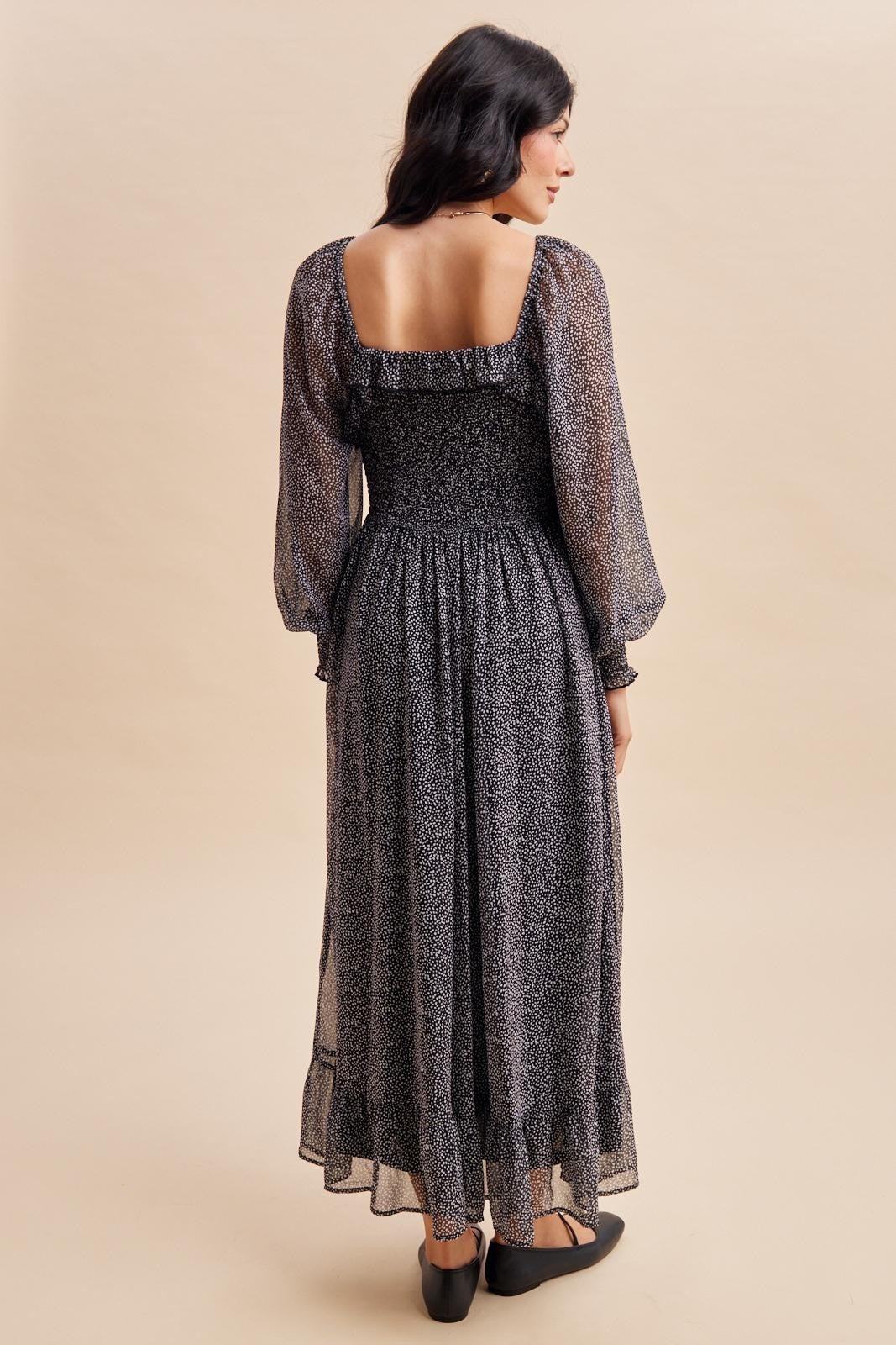 woman wearing a black and white long sleeve maxi dress with a smocked bodice and ruffled neckline, seen from the back