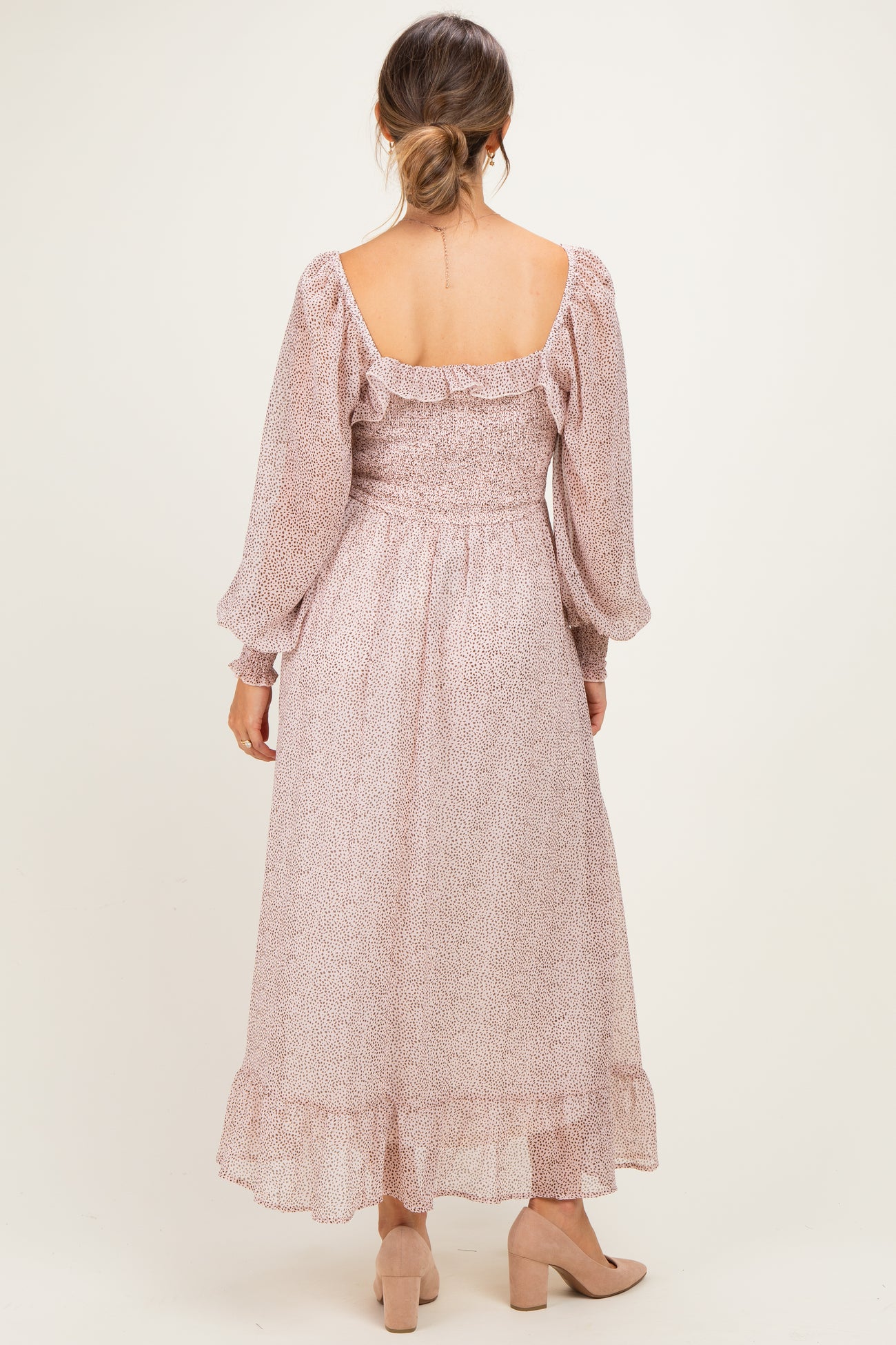 woman wearing a blush floral print maternity dress with long sleeves and a flowy hem, showing a baby bump from the back