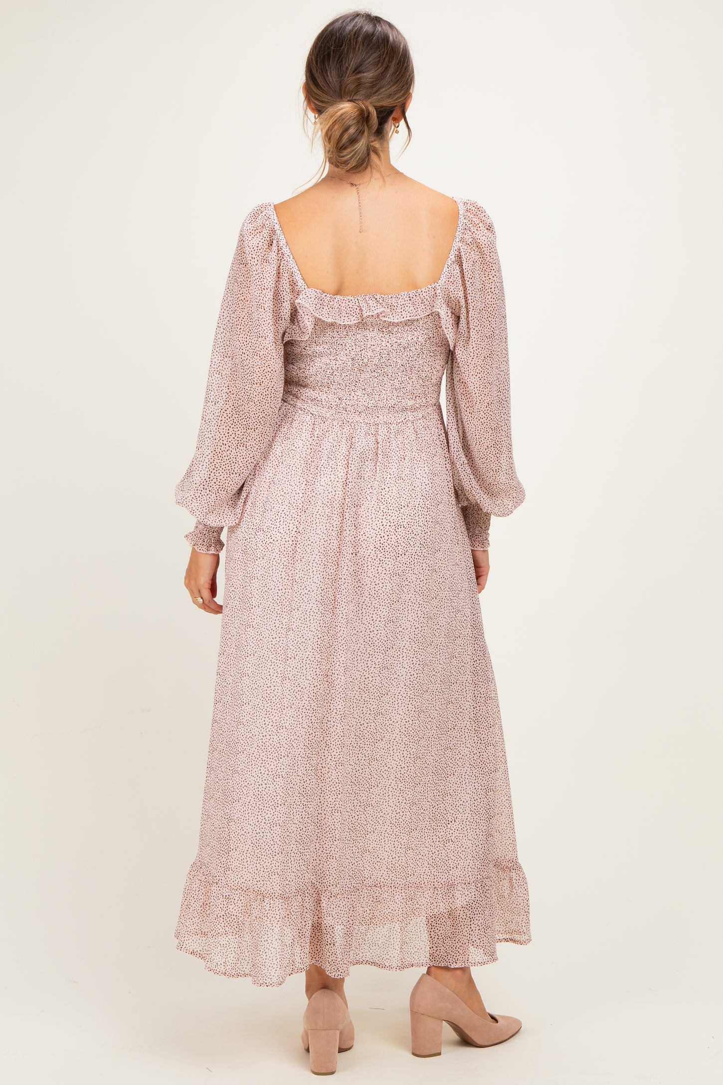 woman wearing a blush floral print maternity dress with long sleeves and a flowy hem, showing a baby bump from the back