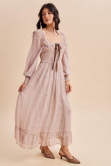 woman wearing a blush floral print maxi dress with puff sleeves and a bow detail at the neckline, paired with beige mules