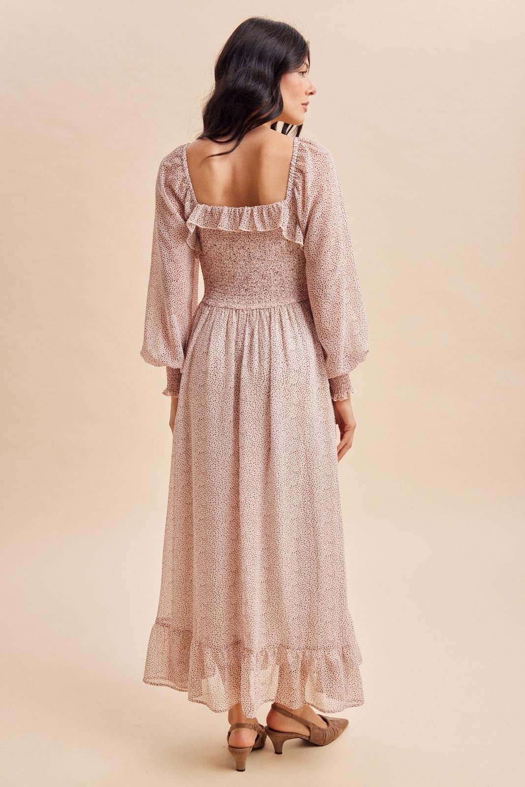 woman wearing a blush pink floral maxi dress with a ruffled neckline and long sleeves, showing the back view