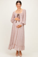 woman wearing a blush floral maternity maxi dress with a square neckline and bow detail, holding her baby bump