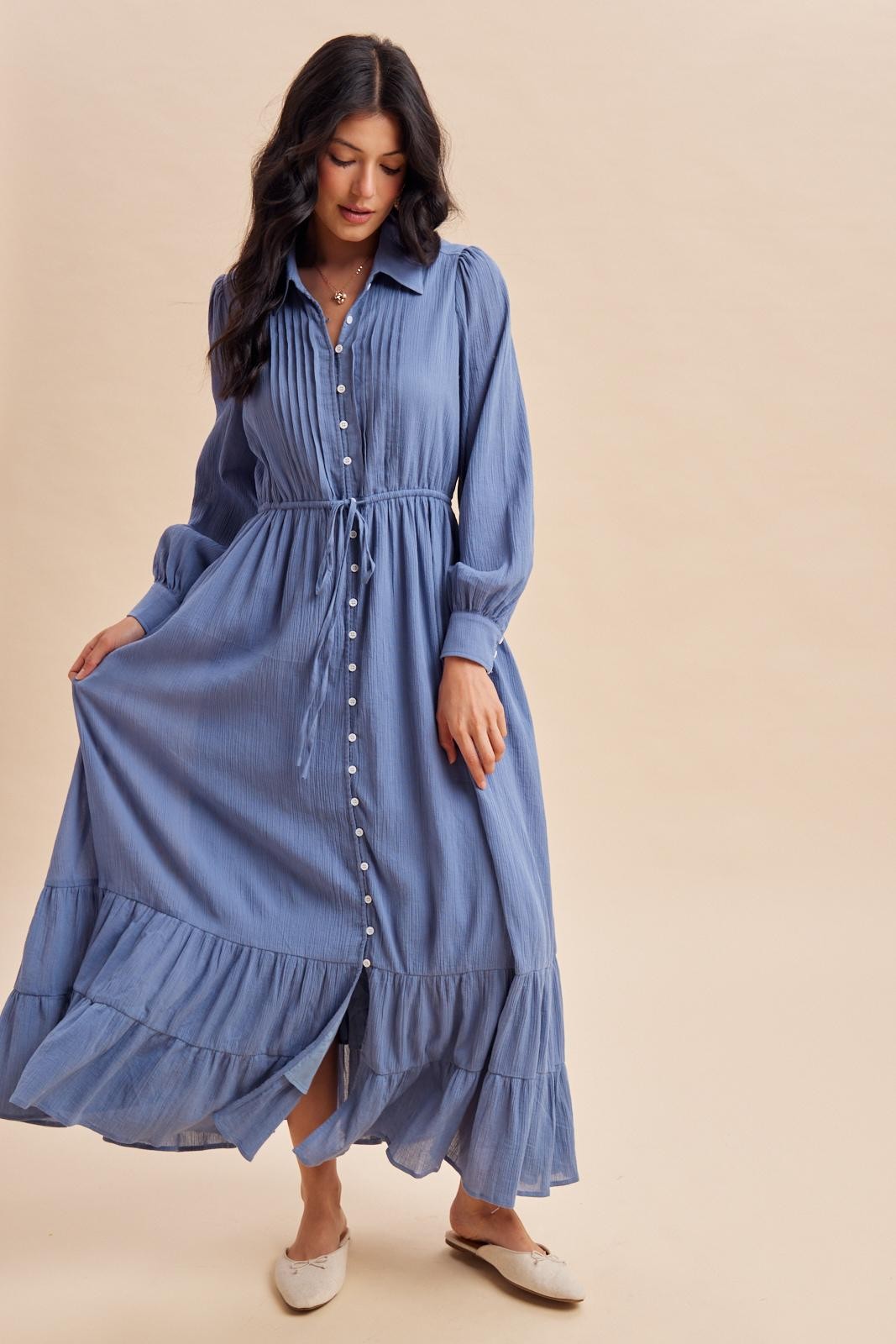 woman wearing a light blue maxi dress with a button-up front and ruffled hem, styled with a tied waist and long sleeves