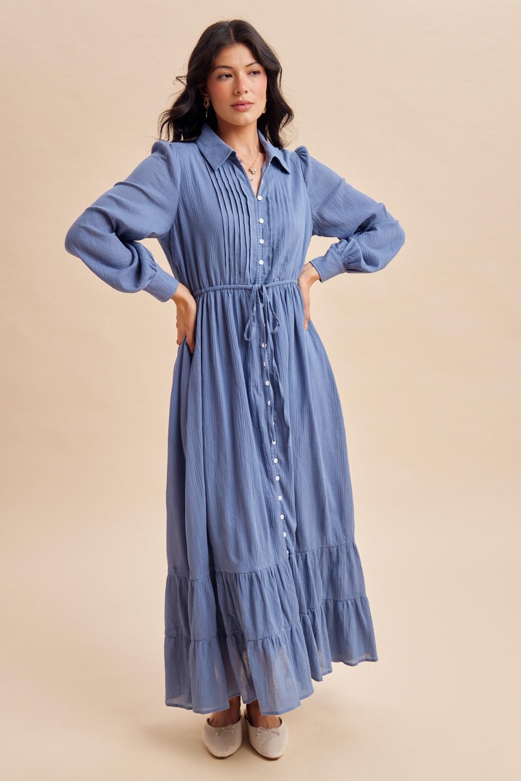 woman wearing a light blue long sleeve button-up maxi dress with a drawstring waist and tiered skirt