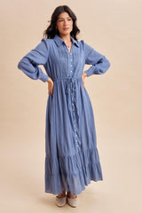 woman wearing a light blue long sleeve button-up maxi dress with a drawstring waist and tiered skirt