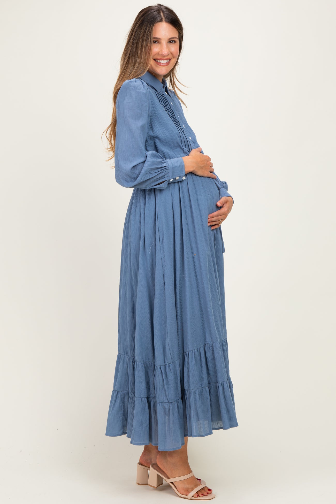 woman wearing a light blue maternity maxi dress with ruffled hem and buttons, cradling her baby bump