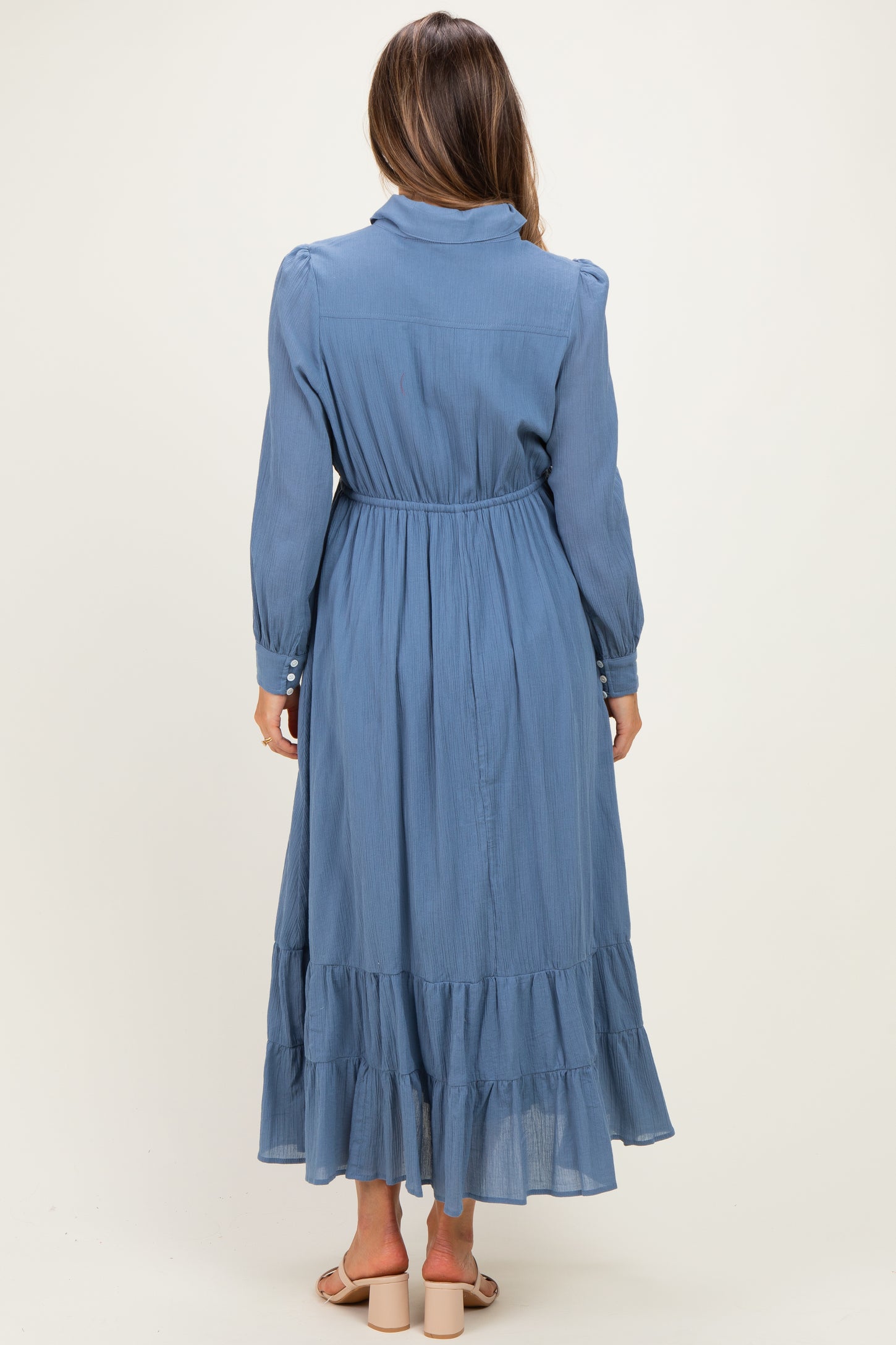 woman wearing a blue long sleeve maternity dress with a ruffled hem and a tie waist, viewed from the back