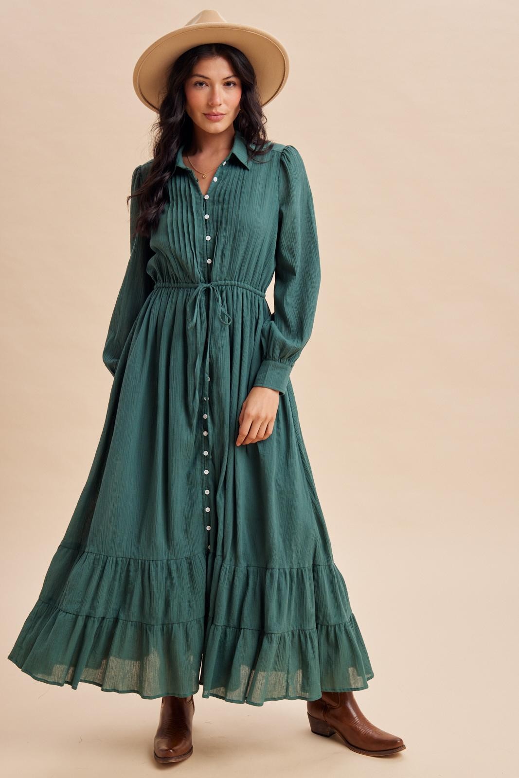 woman wearing a green long sleeve maxi dress with a button front and ruffled hem, styled with a wide-brimmed hat and brown boots