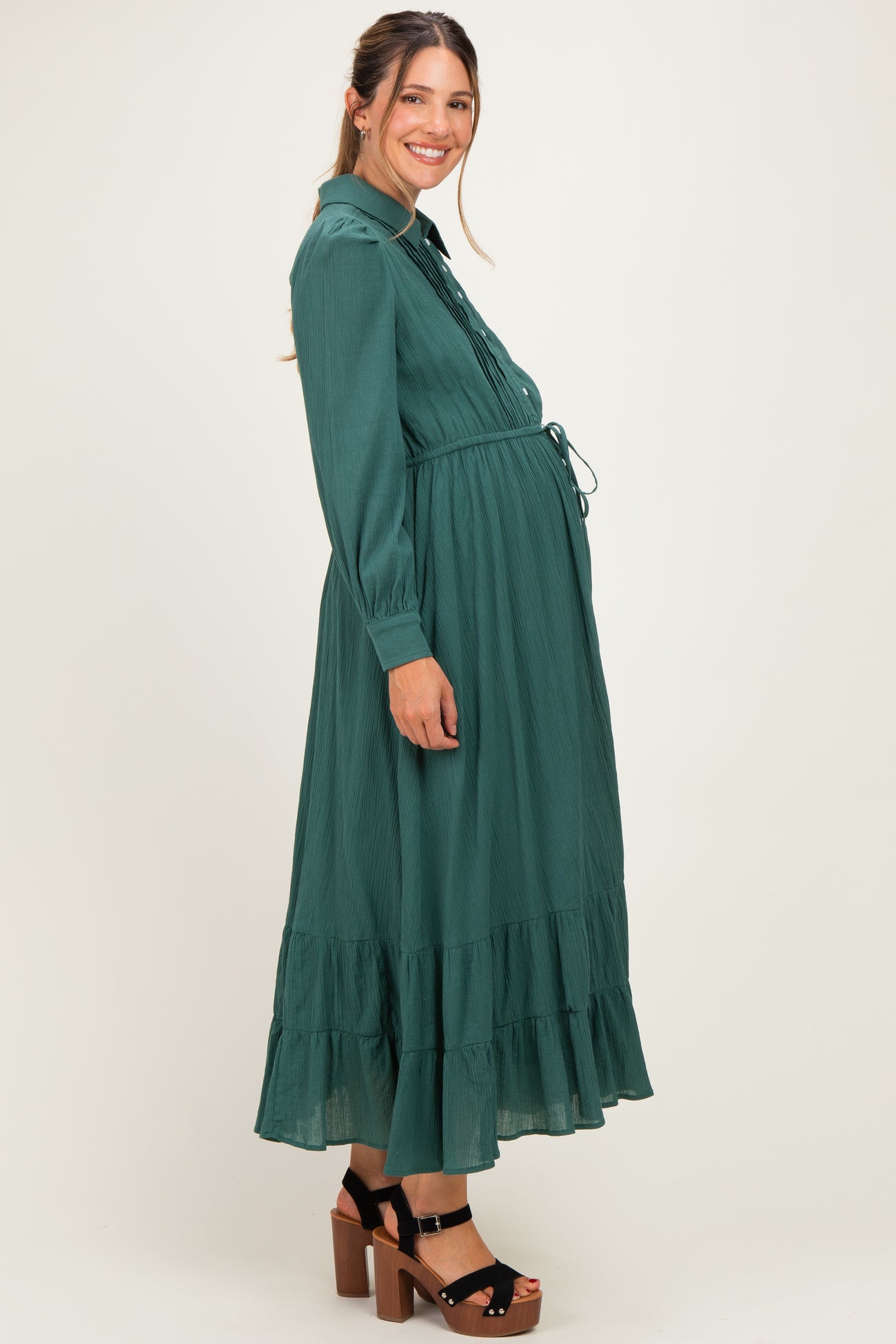 woman wearing a dark green long sleeve maternity dress with a tiered skirt and visible baby bump