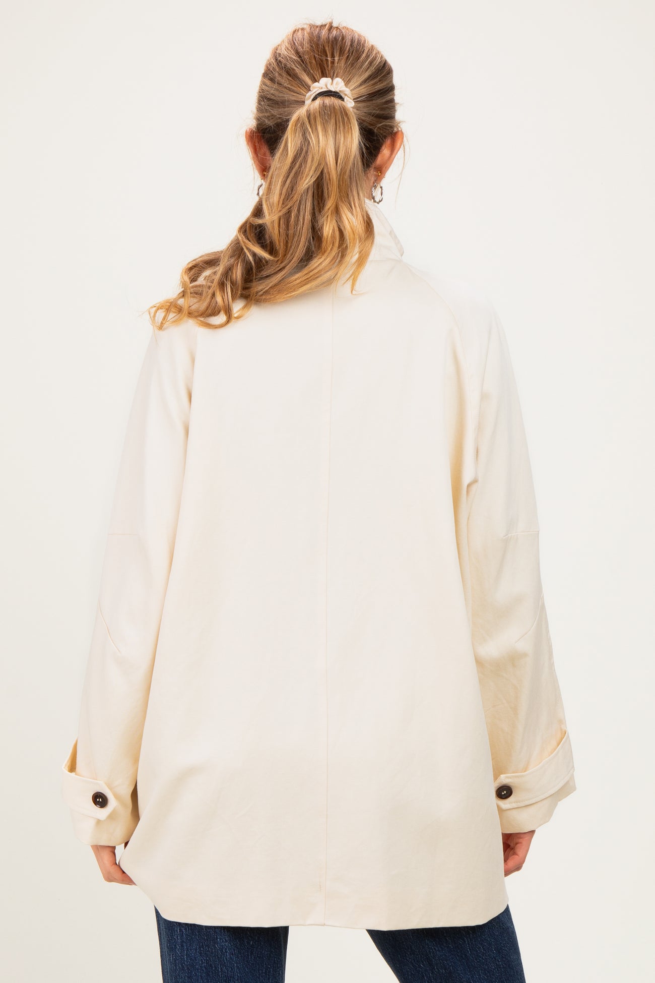 woman wearing a beige oversized maternity jacket with a relaxed fit, styled with rolled sleeves and back facing camera