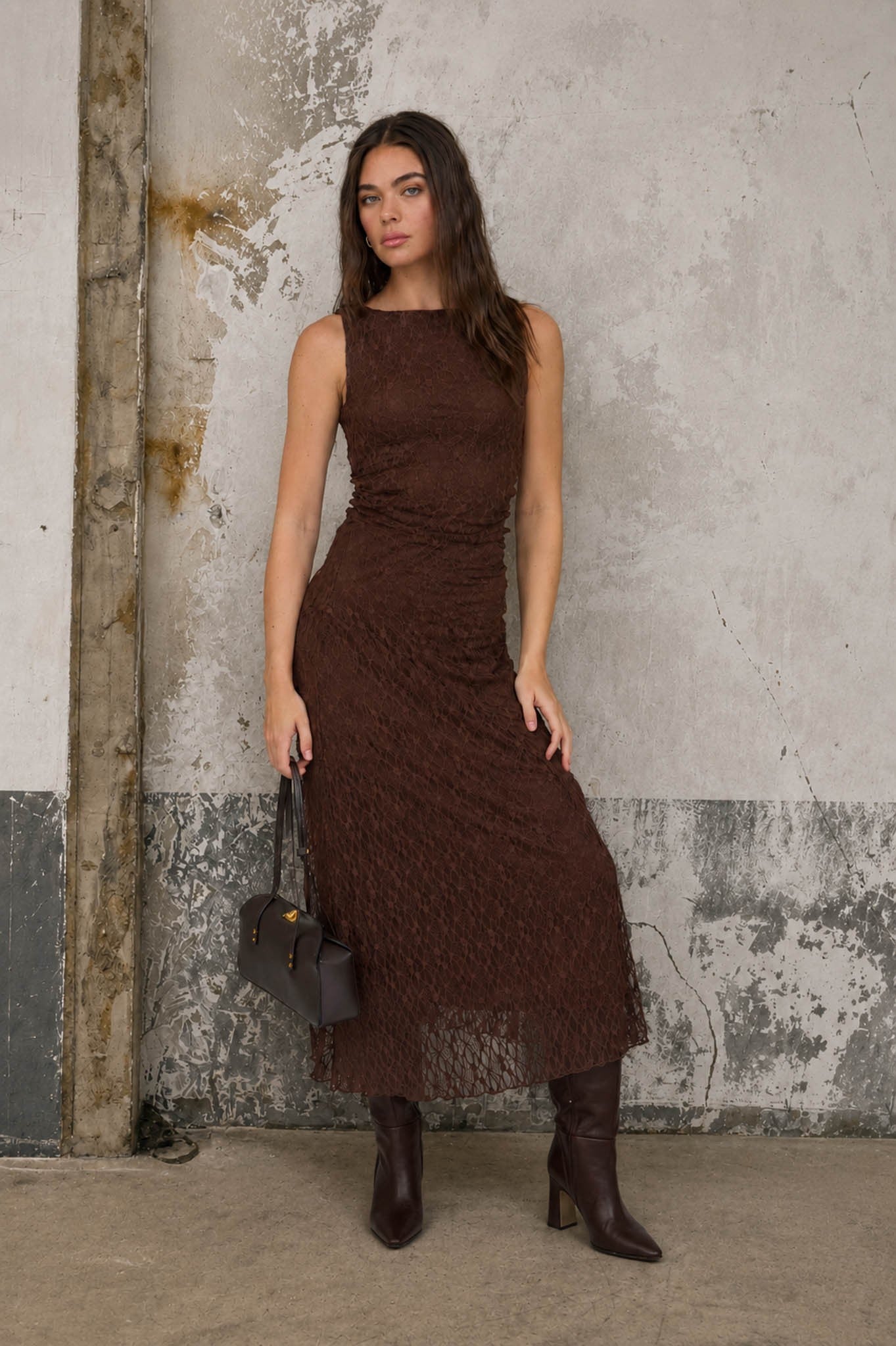 woman wearing a brown lace midi dress with a fitted silhouette and long dark boots, holding a small handbag