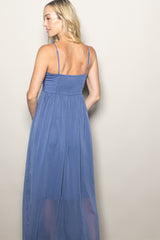 woman wearing a blue sleeveless maxi dress with a smocked back and a flowy skirt, viewed from the back