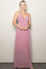 woman wearing a light pink halter maxi dress with a gathered bodice and flowing skirt
