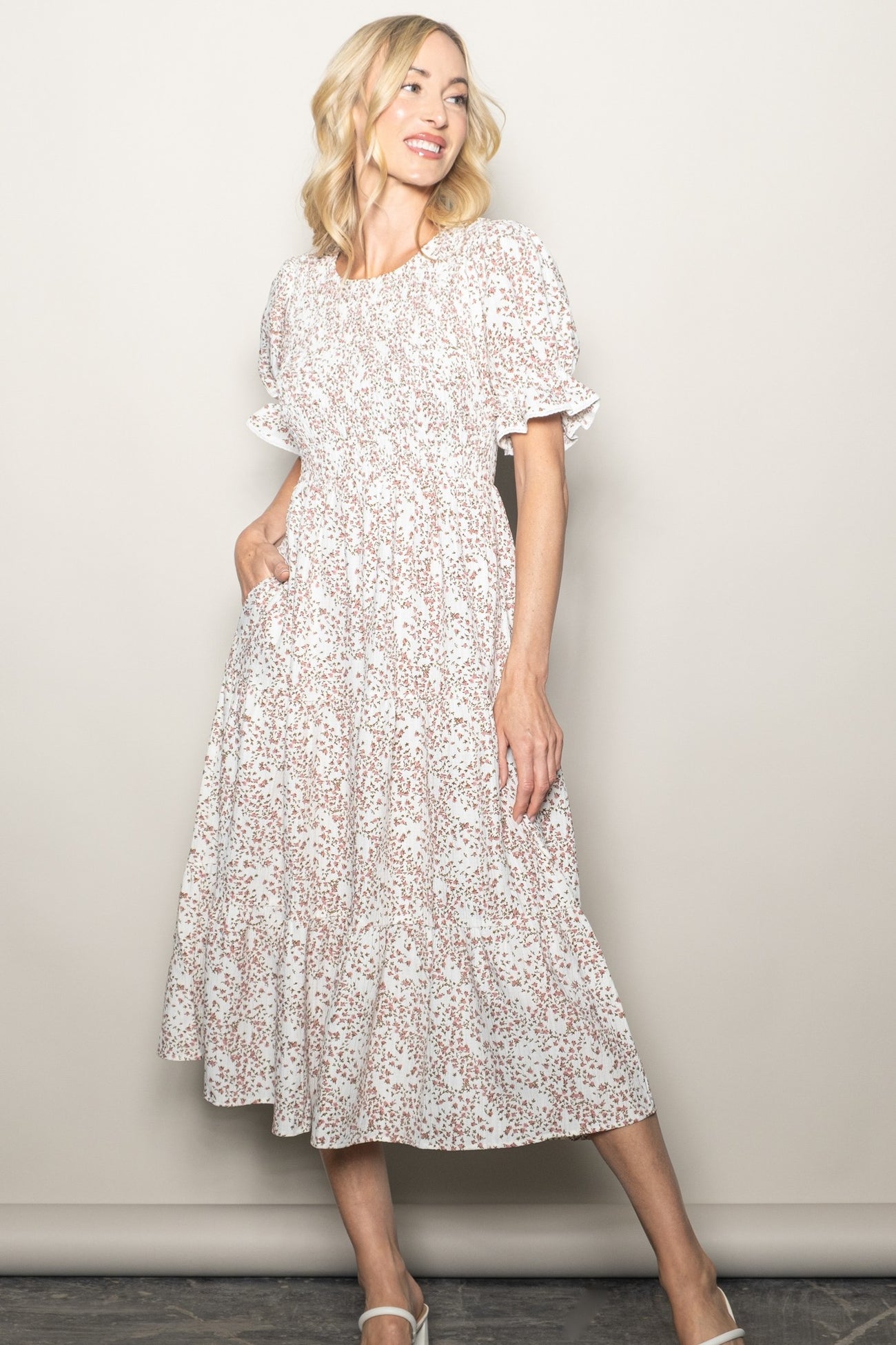 woman wearing a white floral midi dress with puff sleeves and gathered detailing, standing with a smile