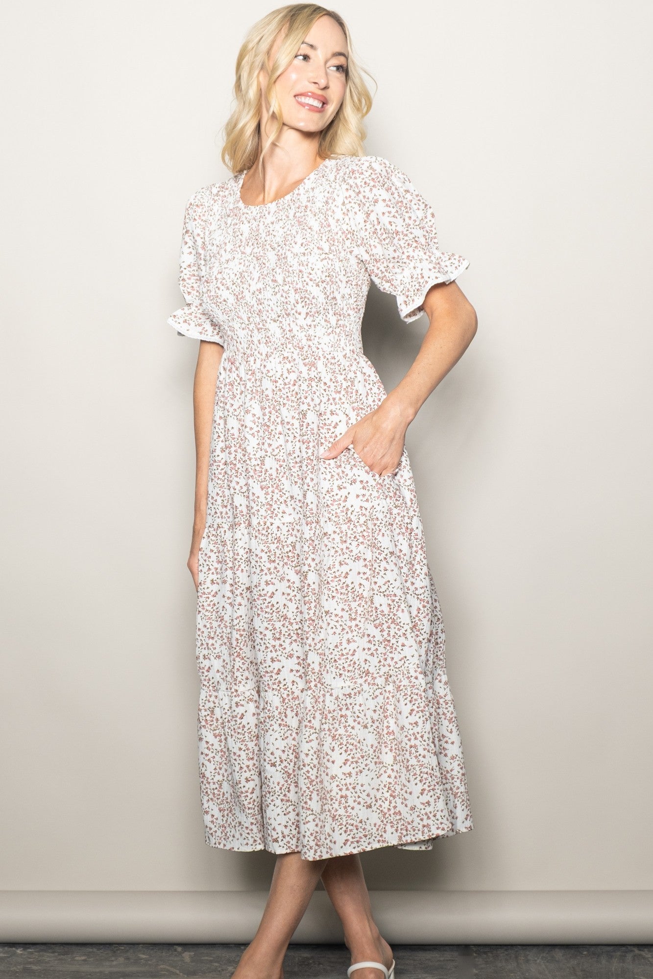 woman wearing a floral print midi dress with short puff sleeves and side pockets, smiling against a neutral background