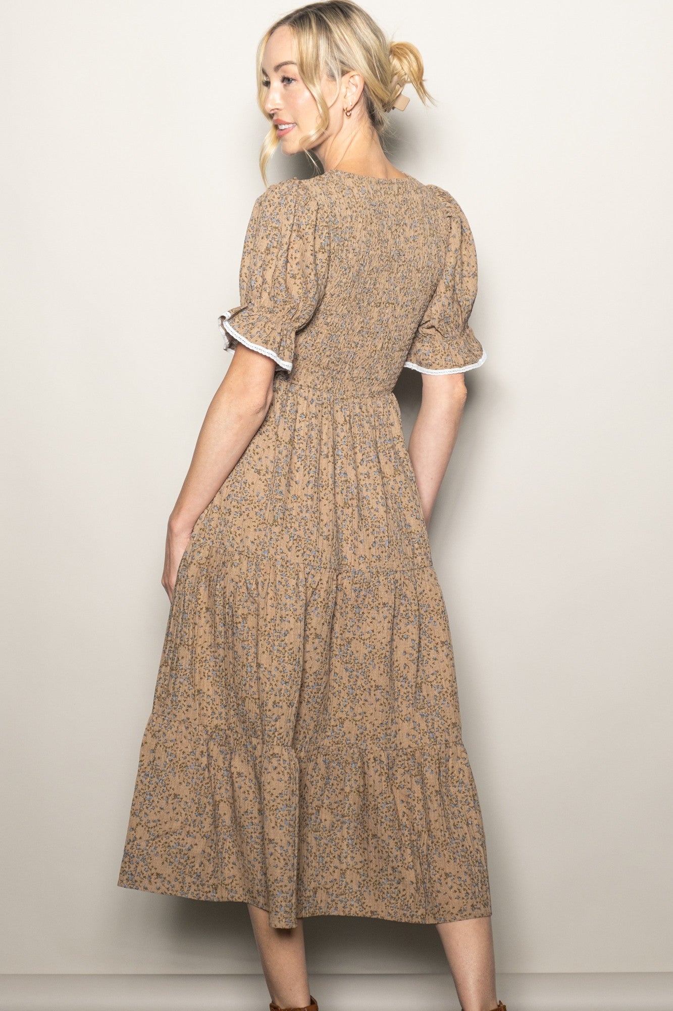 woman wearing a brown floral midi dress with puff sleeves and a tiered skirt, posed from the back
