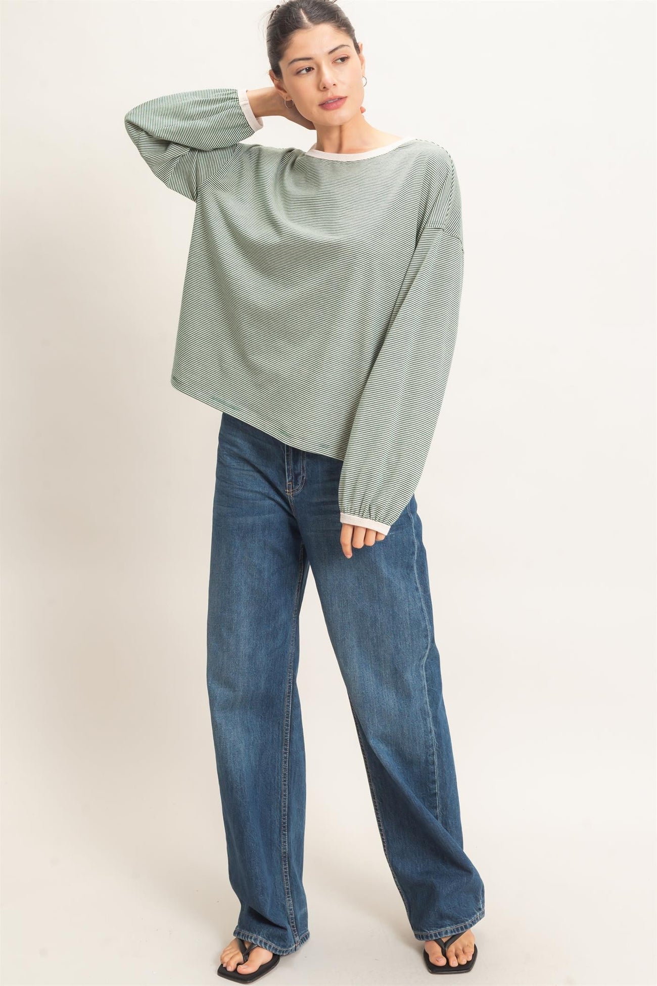 woman wearing a green striped long sleeve oversized top and blue wide-leg jeans