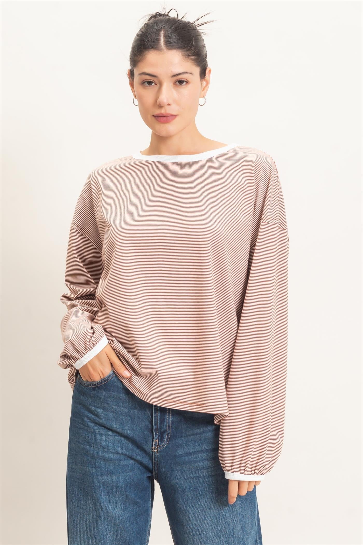 woman wearing a light brown striped long sleeve top with a relaxed fit and ribbed cuffs, paired with blue jeans