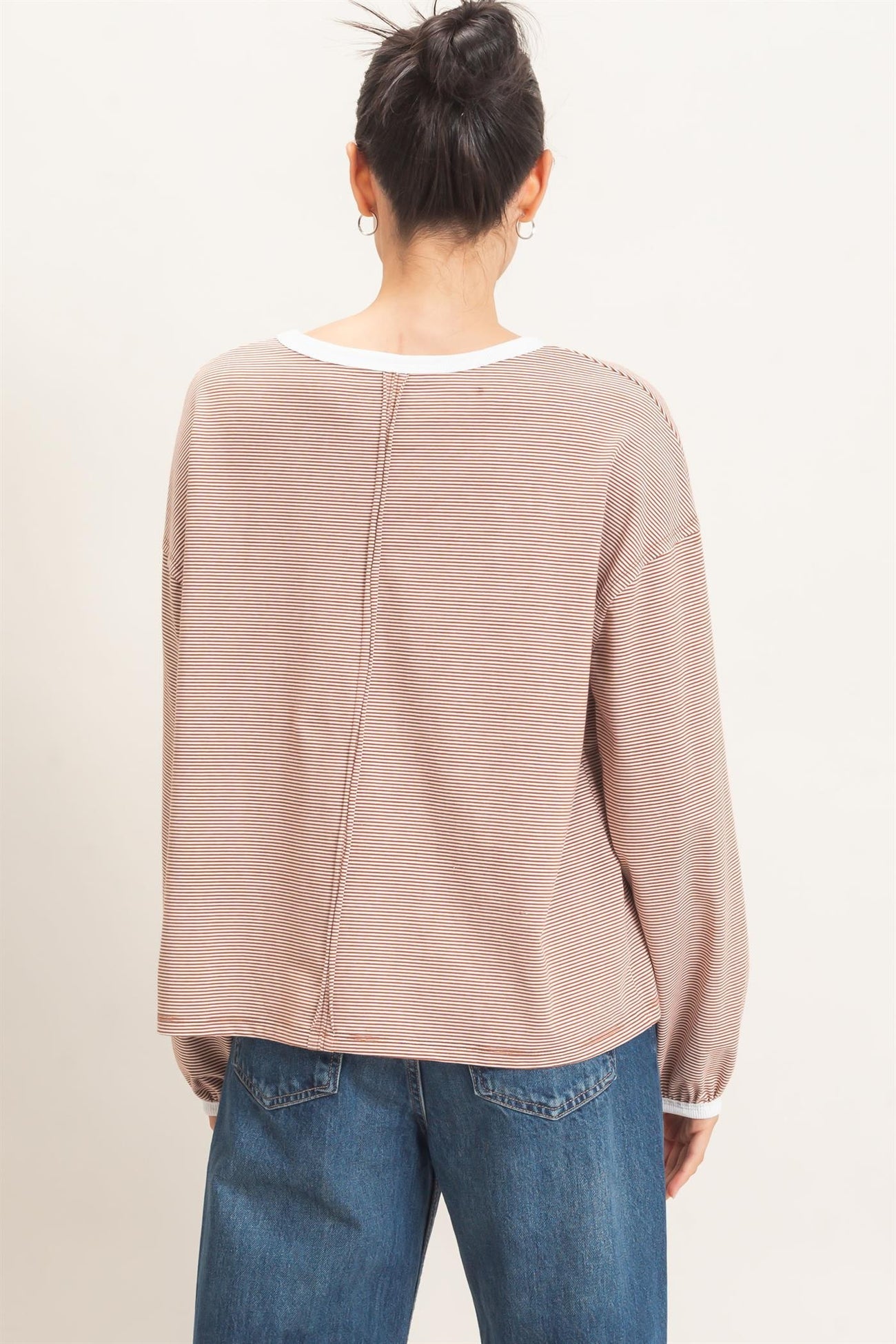 woman wearing a beige striped oversized sweater with a white neckline and back seam, styled with high-waisted blue jeans