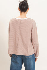 woman wearing a beige striped oversized sweater with a white neckline and back seam, styled with high-waisted blue jeans