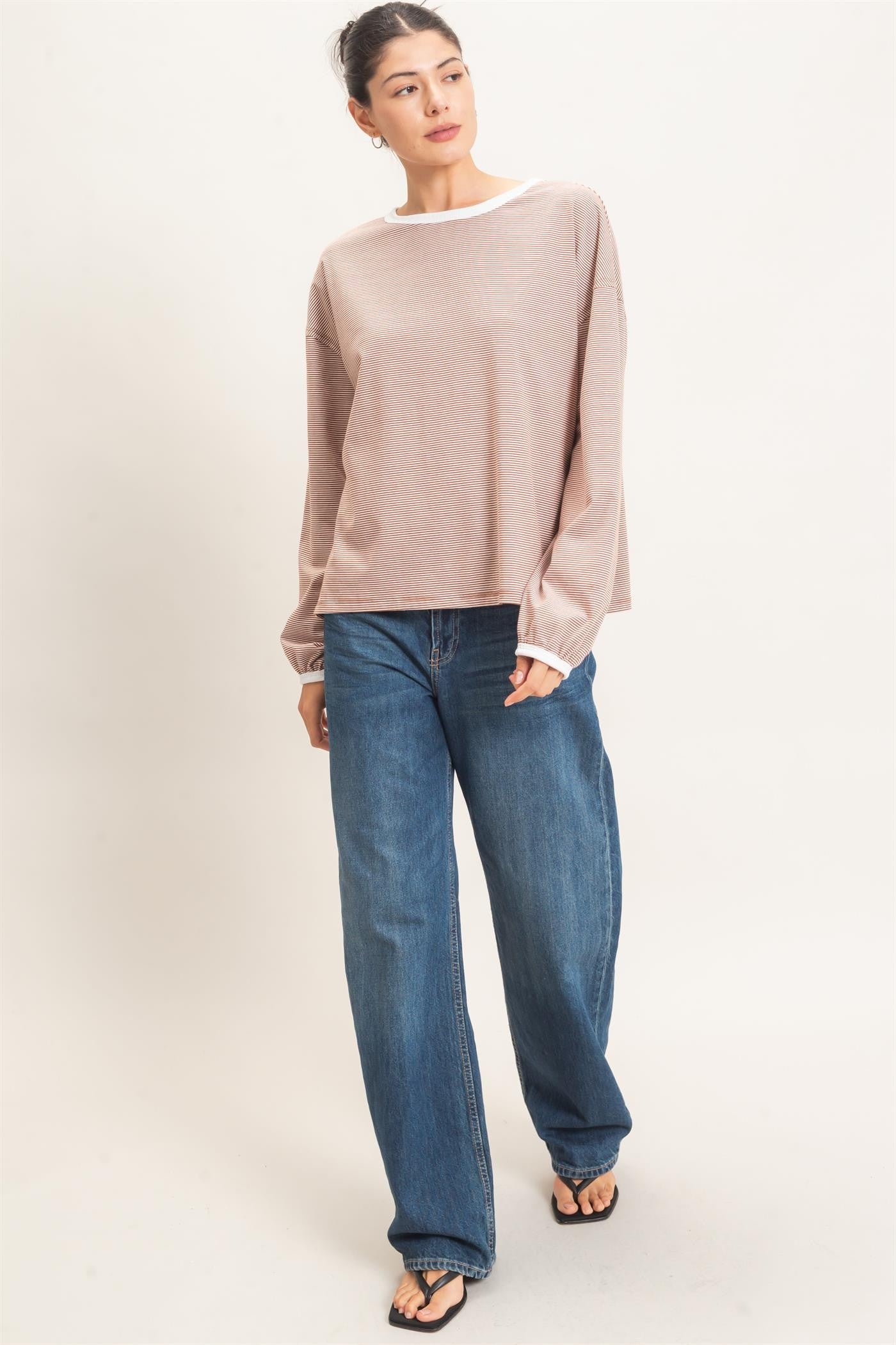 woman wearing a light taupe long sleeve top with white trim and loose blue jeans