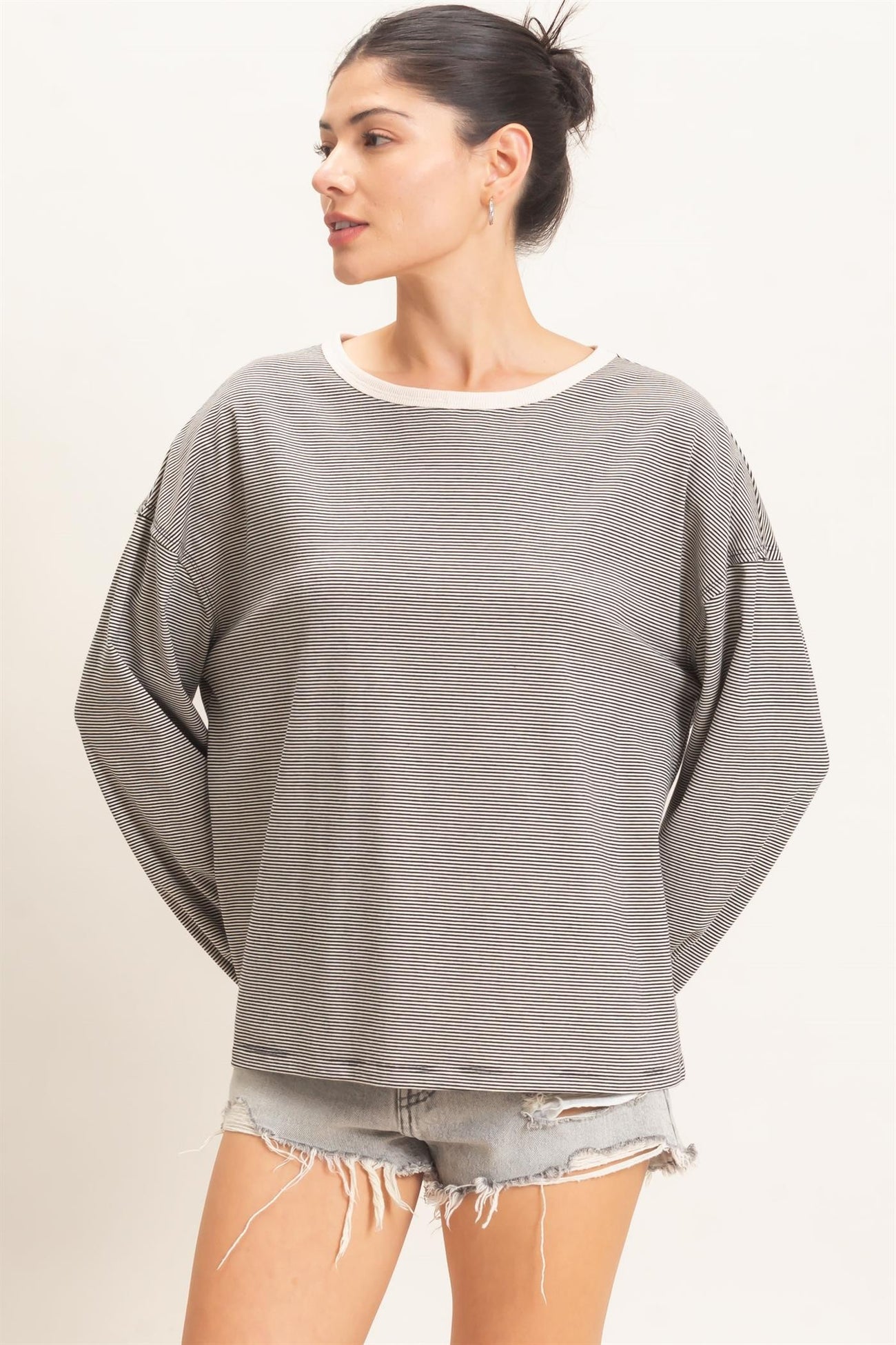 woman wearing a gray and white striped oversized sweatshirt with rolled cuffs and distressed denim shorts