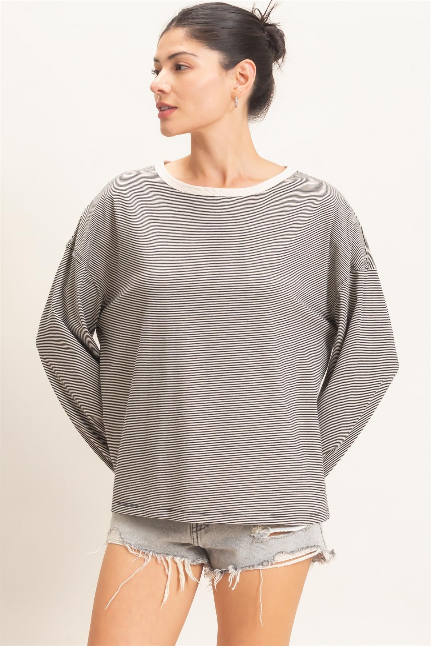 woman wearing a gray and white striped oversized sweatshirt with rolled cuffs and distressed denim shorts