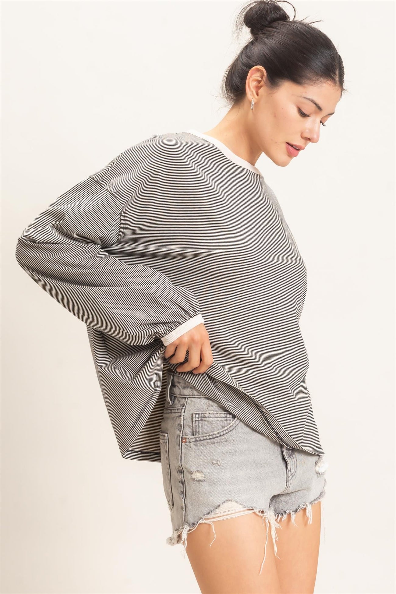 woman wearing a gray striped oversized sweatshirt with white trim and distressed denim shorts