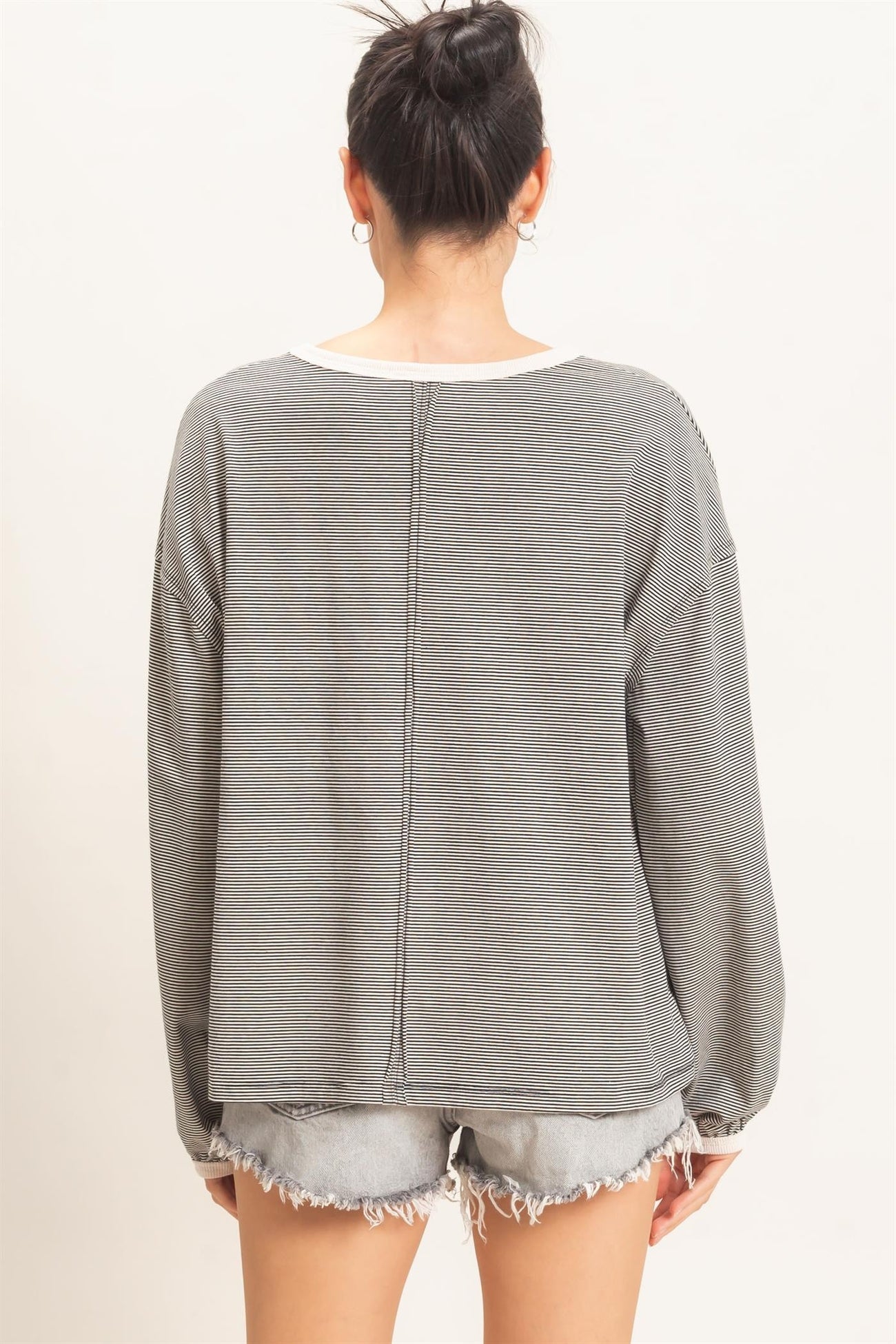 woman wearing a gray striped oversized long sleeve top with a relaxed fit, paired with distressed denim shorts