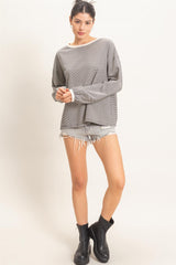 woman wearing a loose gray striped long sleeve top with ripped denim shorts and black ankle boots