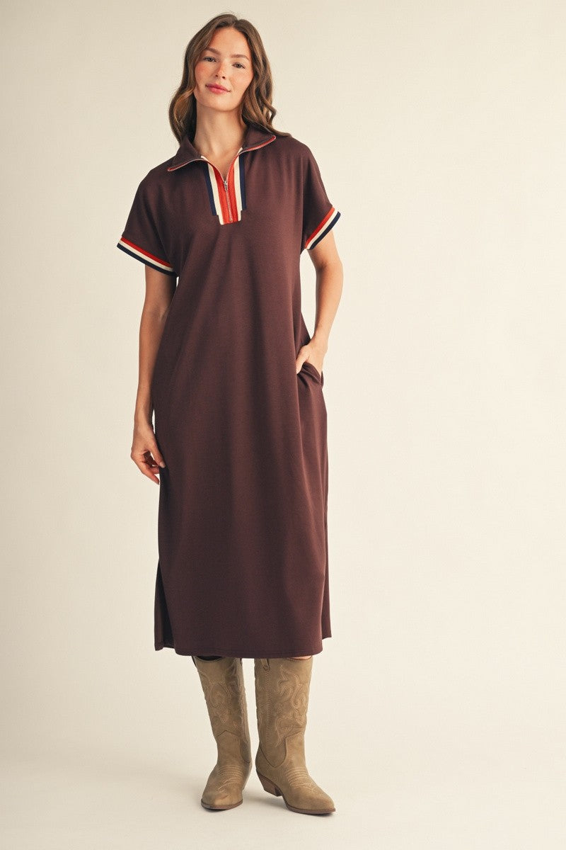woman wearing a brown midi dress with a collar and striped details, paired with tan cowboy boots and standing with hands in pockets