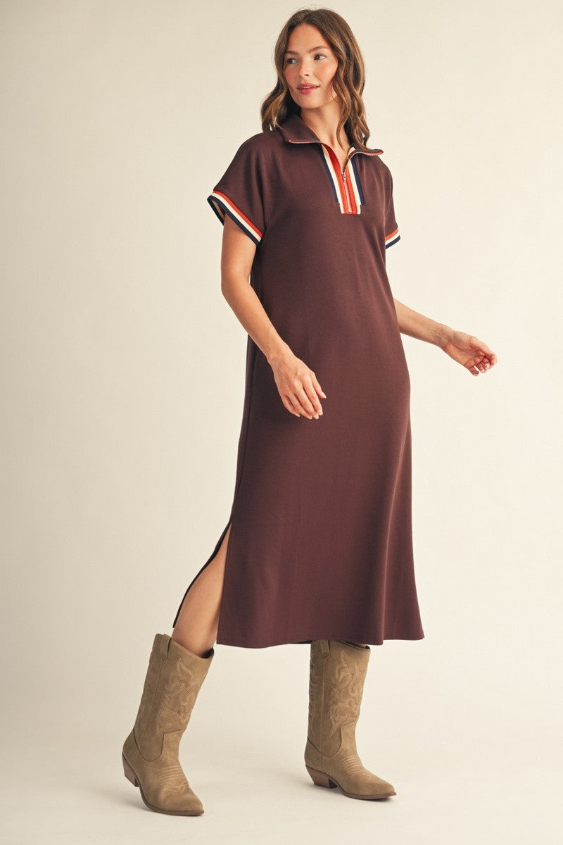 woman wearing a brown polo style dress with striped accents on the sleeves and side slits, paired with tan cowboy boots