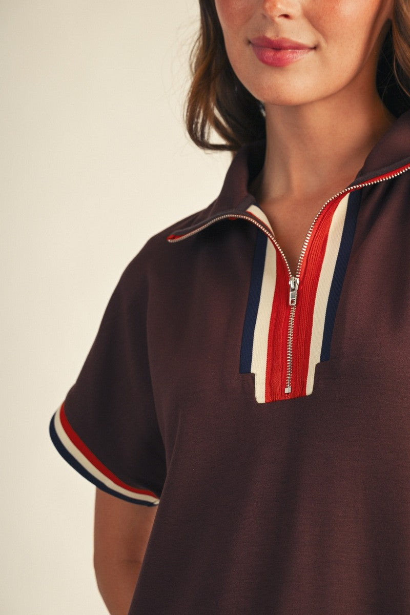 woman wearing a brown short sleeve polo top with a zip neckline and colorful striped details on the sleeves
