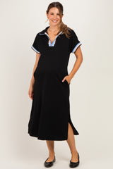 woman wearing a black maternity polo dress with blue collar details and side slits, smiling and posing with hands in pockets