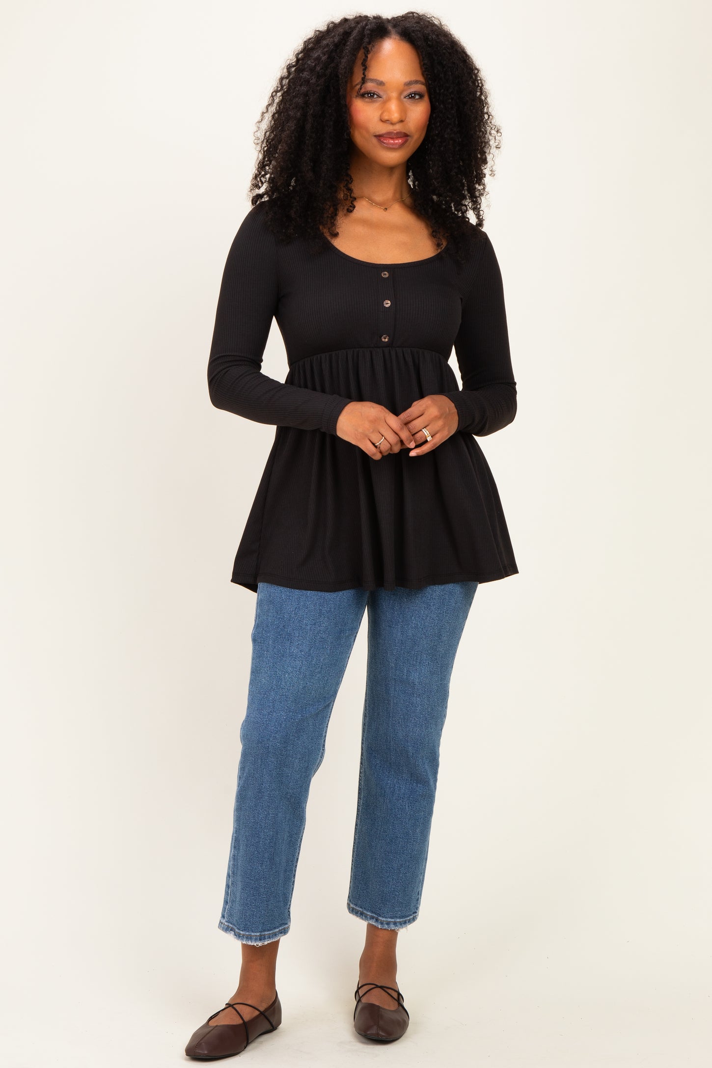 woman wearing a black long sleeve peplum top with button details and blue high-waisted jeans
