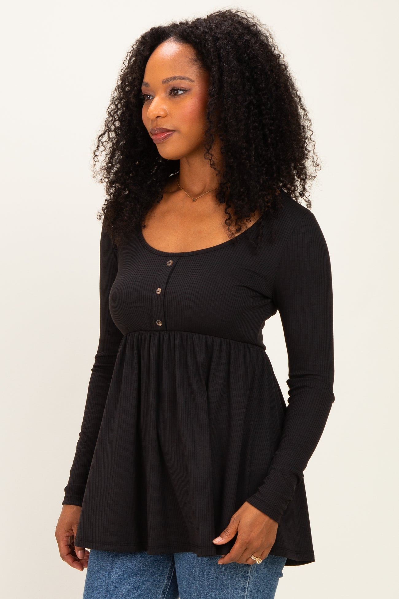 woman wearing a black long sleeve top with a scoop neck and button details, styled with a flared hem