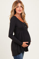 woman wearing a black long sleeve maternity top with buttons and a flared hem, holding her baby bump