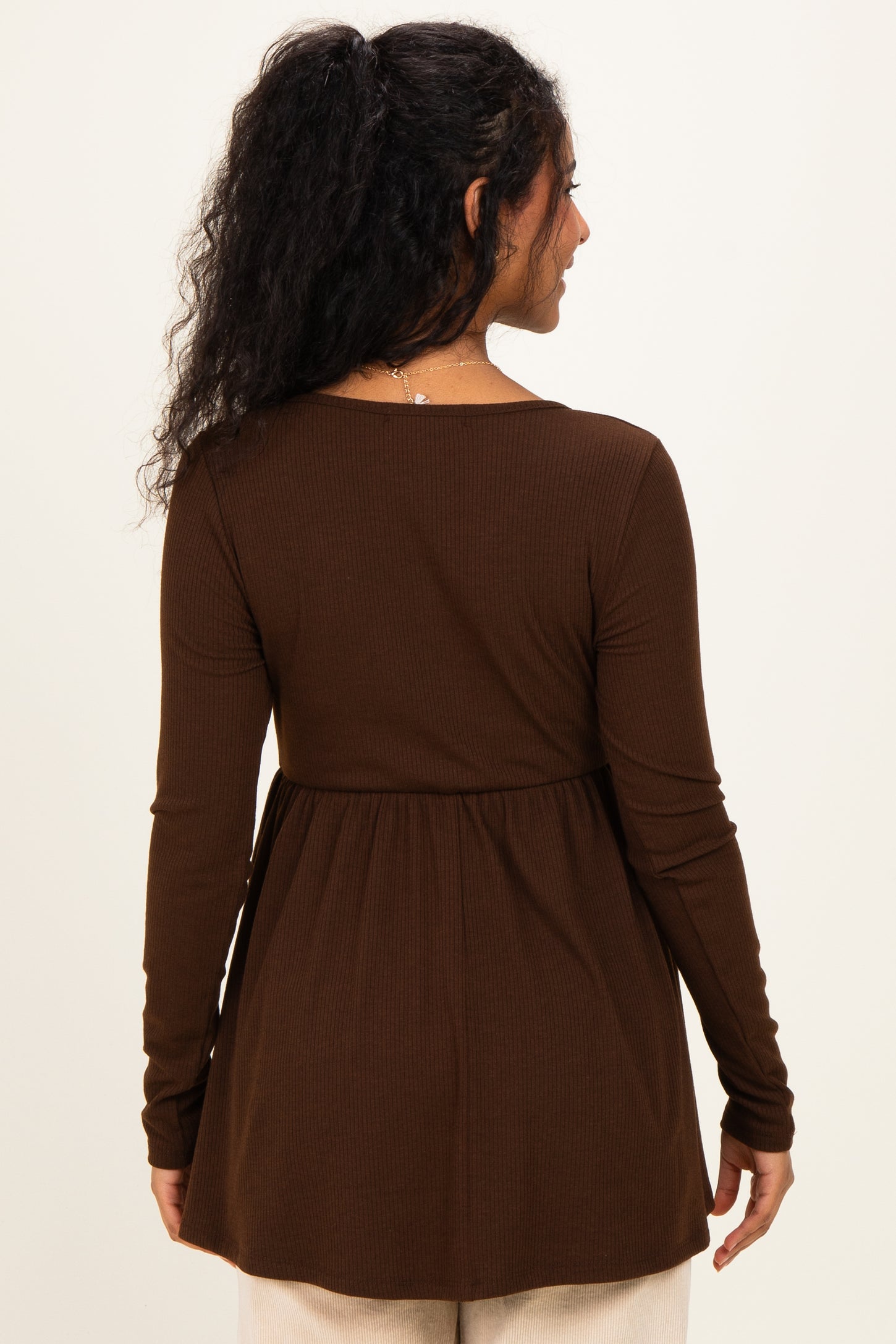 woman wearing a brown long sleeve maternity top with a peplum style and a relaxed fit from the back
