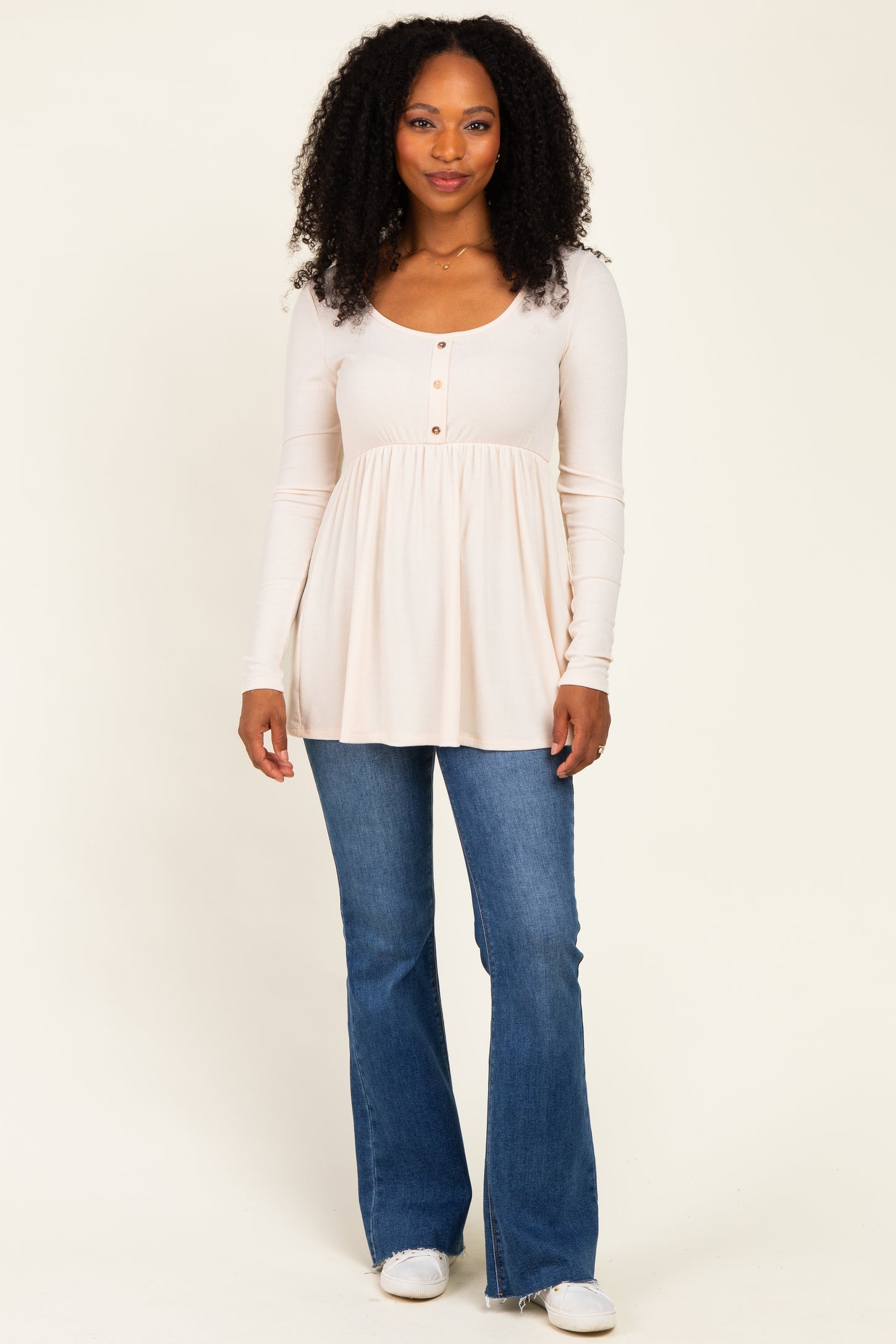 woman wearing a light beige long sleeve top with buttons and a flared hem, paired with blue jeans