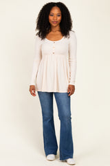 woman wearing a light beige long sleeve top with buttons and a flared hem, paired with blue jeans
