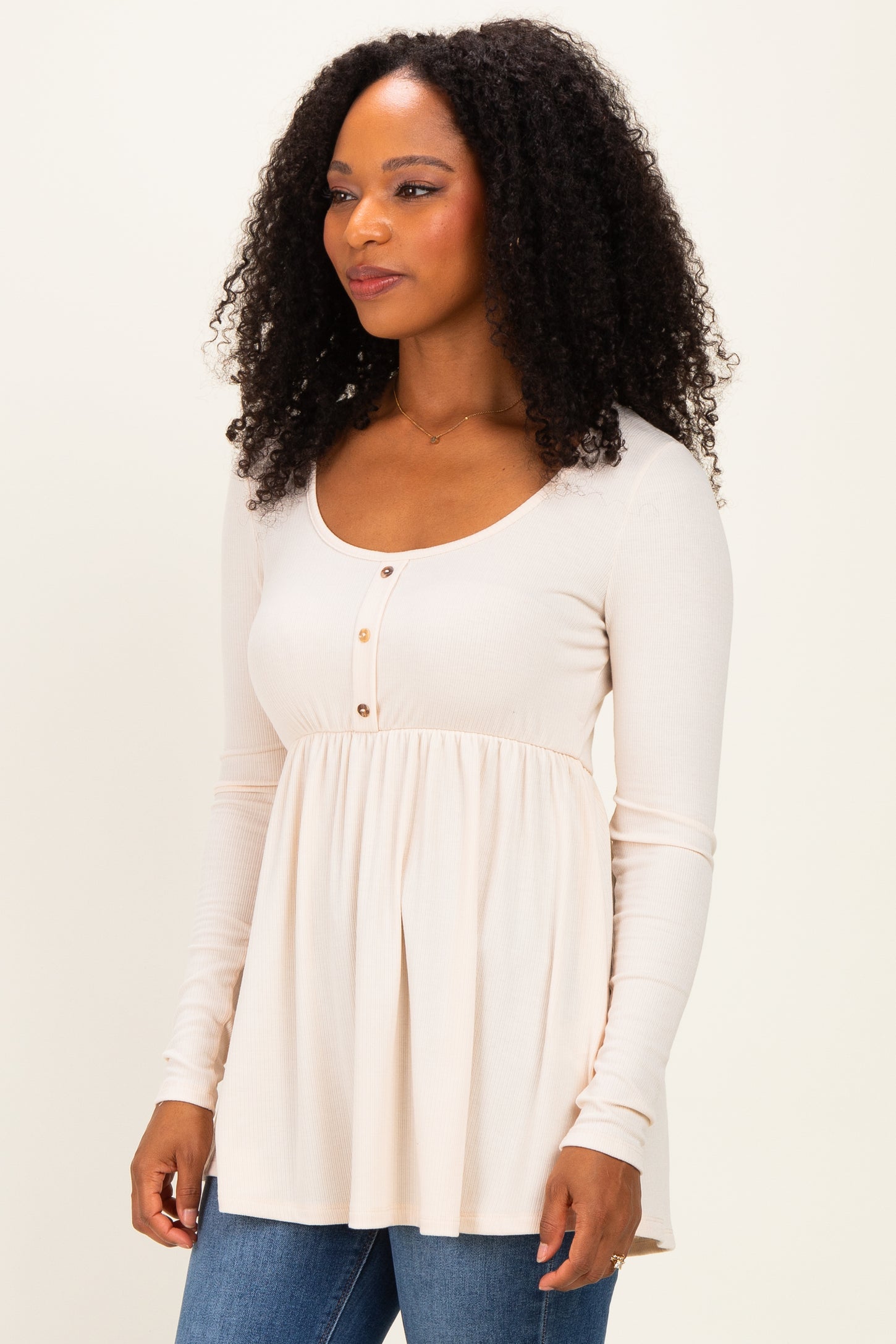 woman wearing a light beige long sleeve top with a scoop neckline and button detail, paired with blue jeans