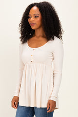 woman wearing a light beige long sleeve top with a scoop neckline and button detail, paired with blue jeans