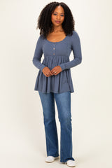 woman wearing a blue long sleeve peplum top with button details and flared jeans, standing against a neutral background
