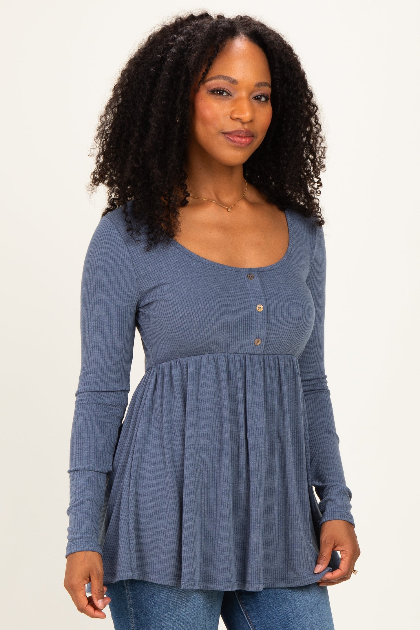 woman wearing a blue long sleeve peplum top with buttons and a scoop neckline, styled with jeans