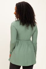 woman wearing a green ribbed long sleeve top with a peplum waist, turned to the side showing the back view