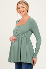 woman wearing a sage green long sleeve maternity top with button details and a gathered waist, showcasing her baby bump