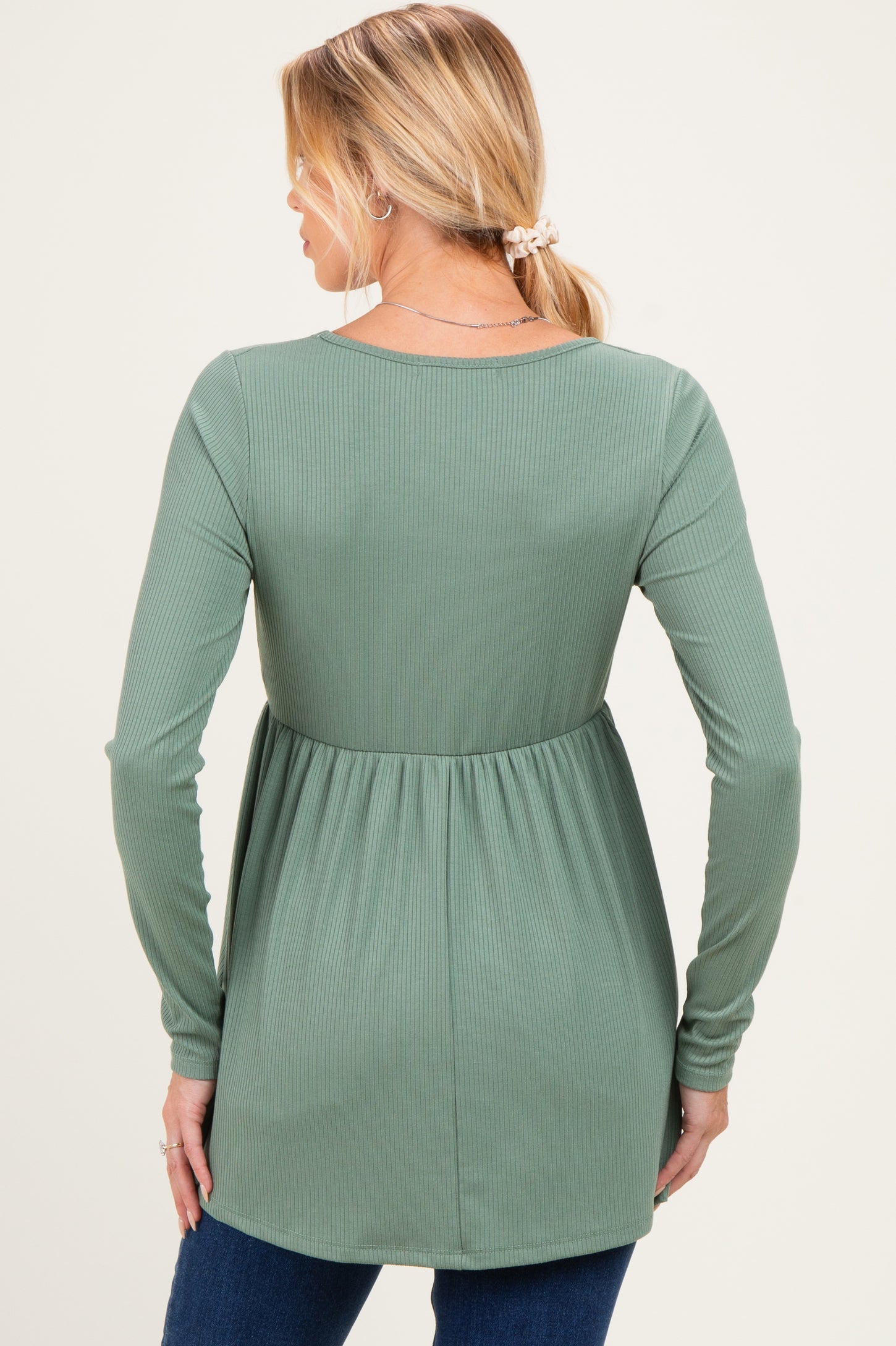 woman wearing a green long sleeve maternity top with a flowy hem and ribbed texture, showing a baby bump from the back