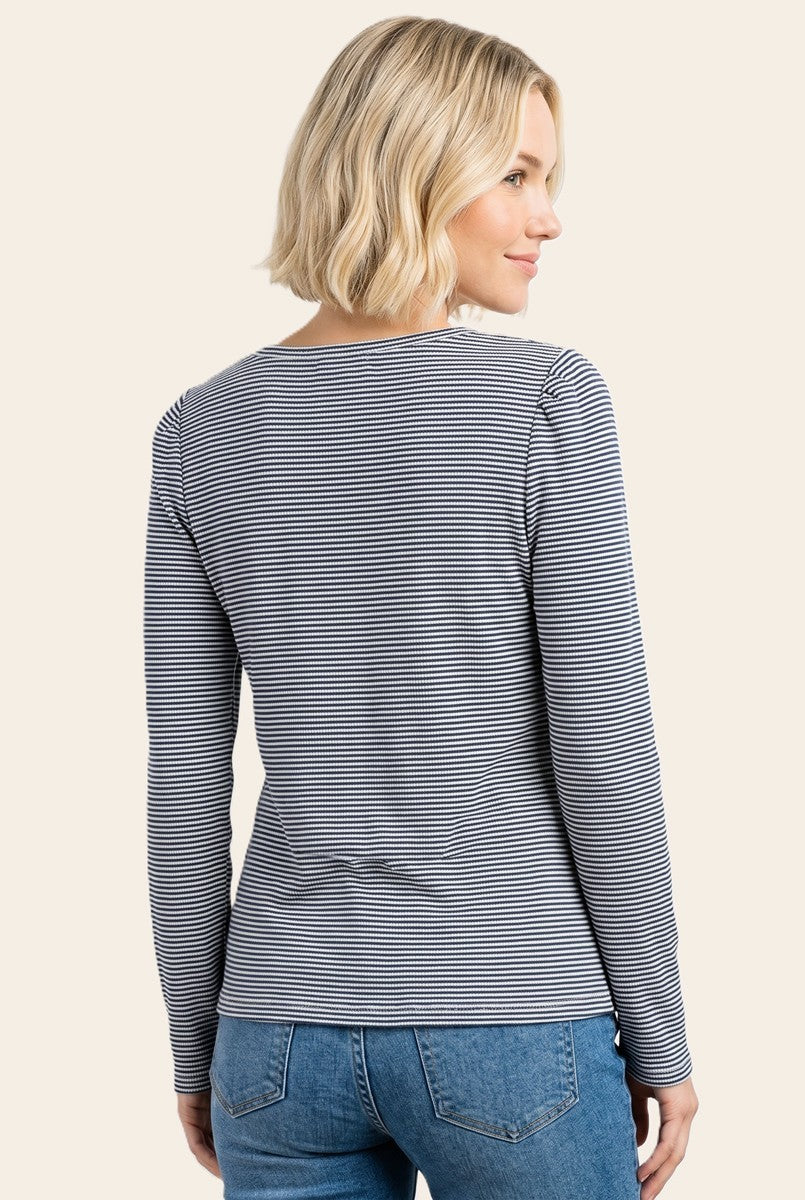 woman wearing a fitted long sleeve striped top, viewed from the back, paired with blue jeans