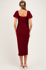 woman wearing a burgundy maternity dress with puff sleeves and a midi length, showing a fitted silhouette from the back